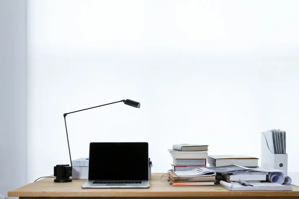 Laptop auf einem Schreibtisch neben gestapelten Büchern